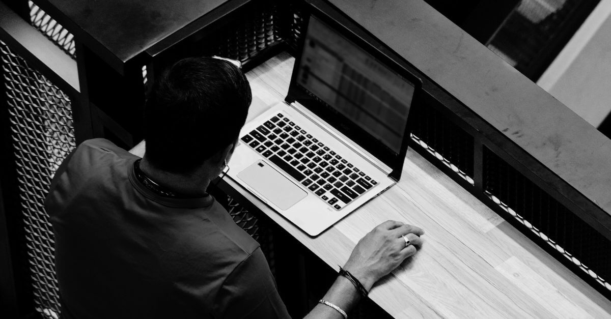 Homem sentado em uma escrivaninha, com um notebook olhando para um planilha.