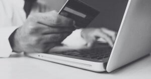 imagem de uma pessoa segurando um cartão de crédito em frente ao computador fazendo uma compra online.